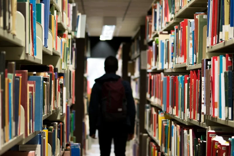 学生背着书包走过图书馆的书架走道